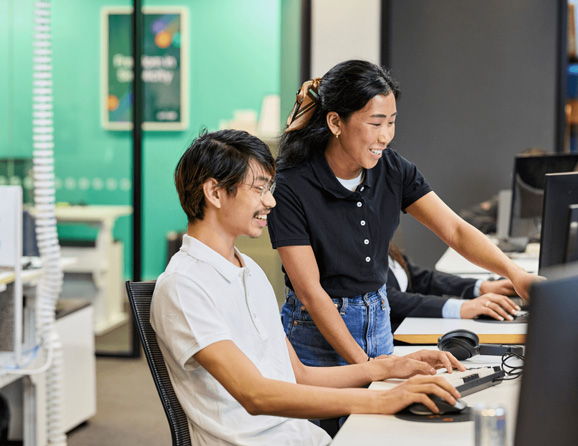 Two Prvidr staff looking at a computer screen smiling. One it sitting, the other is standing and pointing at the screen.